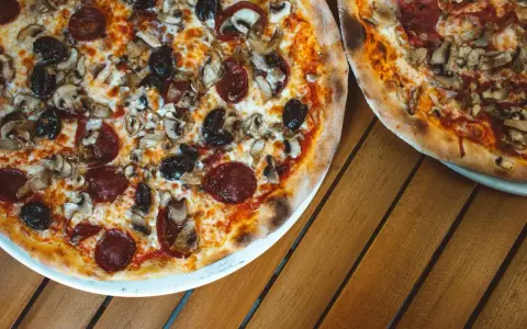 Dwie pizze z bogactwem składników na wierzchu: salami, pieczarki i czarne oliwki. Idealne na wspólny posiłek.