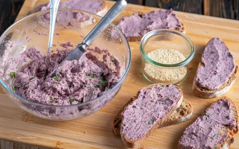 Pyszna pasta z czerwonej fasoli na chlebie, obok słoiczek sezamu. Idealna na szybką przekąskę.
