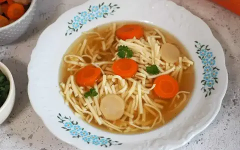 Aksamitny rosół z kaczki z makaronem nitki, marchewką i kawałkami mięsa, ozdobiony natką pietruszki.