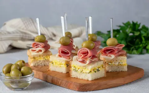 Mini kanapki z szynką, jajkiem i oliwkami na drewnianej desce. Idealne finger food na przyjęcie.
