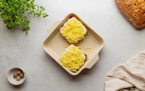 Dwa tosty z serem i beszamelem, przygotowane do zapieczenia jako croque madame. Obok gałka muszkatołowa i świeże zioła.