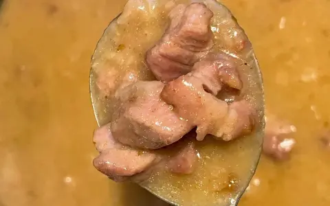 Łyżka pełna aromatycznego sosu z karkówki, z kawałkami mięsa w kremowym sosie.
