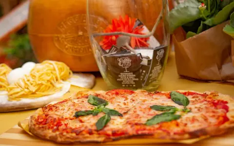 Pyszne rodzaje pizzy, makaron i ser parmezan. W tle szklany wazon z ozdobami i kwiatami.