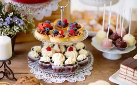 Słodkie przekąski: babeczki, tartaletki z owocami, cake pops i ciasto czekoladowe na drewnianym stole.