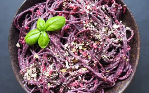 Fioletowy makaron z buraczanym pesto ze słoika, posypany orzechami i udekorowany listkiem bazylii.