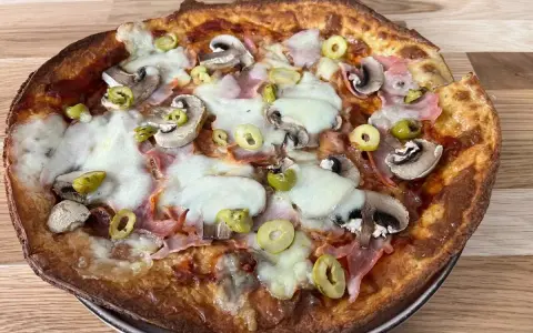 Apetyczna pizza z twarogu z pieczarkami, szynką i oliwkami, z ciągnącym się serem.