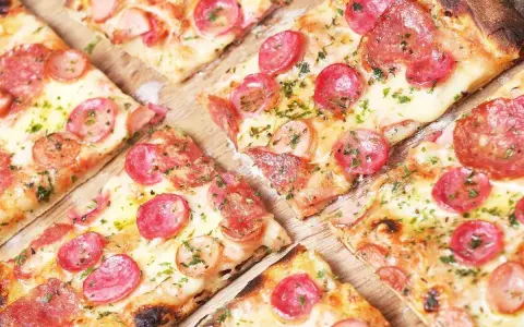 Kawałki pysznej pizzy cienkie ciasto z kiełbasą i serem, posypane ziołami. Idealna na szybką przekąskę.