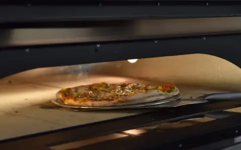 Pieczenie pizzy w piecu. Czy pizzę można zamrozić? Ta gorąca, parująca pizza na łopacie sugeruje, że świeżość jest kluczowa.