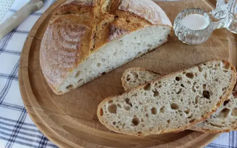 Chleb pszenno żytni na zakwasie, pokrojony na desce, z solniczką i nożem w tle.