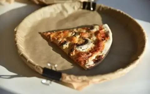 Kawałek pizzy z pieczarkami na brązowym papierze. Zastanawiasz się, ile kalorii ma pizza?