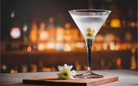 Kryształowy kieliszek z martini, trzema oliwkami i białą kwiatową ozdobą. Idealny drink, z czym pić martini?