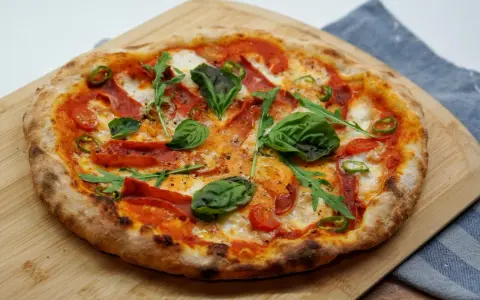 Pyszna pizza z rukolą, pomidorkami, papryczką i salami. Idealne składniki na pizzę, które zachwycą każdego smakosza.