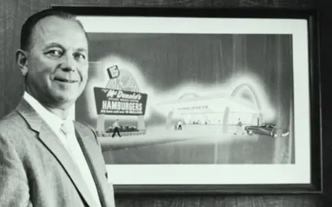Ray Kroc, który wymyślił McDonald's, stoi obok obrazu przedstawiającego pierwszy lokal.