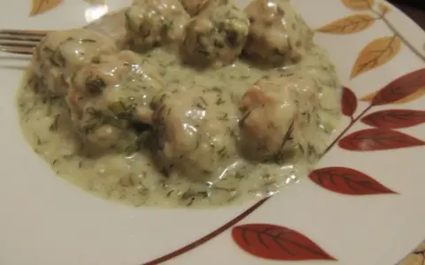 Pyszne klopsiki w sosie koperkowym, podane na talerzu z liśćmi.