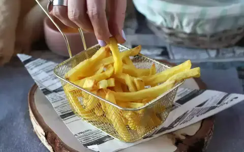 Ręka sięga po chrupiące frytki z koszyka. Idealne do airfryera, by cieszyć się smakiem bez nadmiaru tłuszczu.