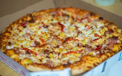 Pyszna, gorąca mrożona pizza w mikrofali, prosto z pudełka. Złocisty ser, kawałki ananasa i papryki kuszą apetycznie.