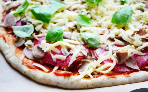 Gotowy do pieczenia przepis na ciasto do pizzy: sos pomidorowy, salami, pieczarki, ser i świeża bazylia.