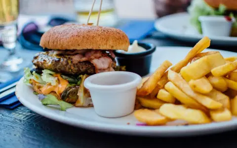 Pyszny burger z bekonem i frytki na talerzu. Idealny sposób, jak jeść burgera w restauracji, by delektować się każdym kęsem.