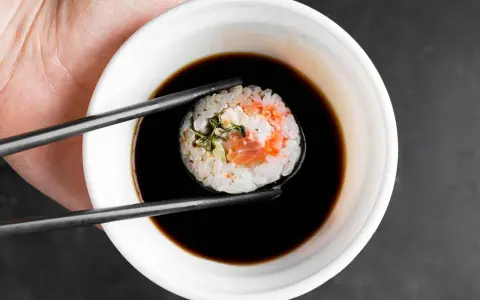 Pałeczki trzymają sushi z łososiem, zanurzając je w ciemnym sosie do sushi.