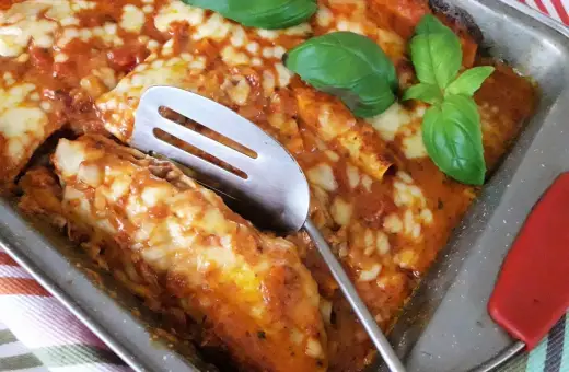 Zapiekana tortilla z mięsem mielonym, polana sosem pomidorowym i posypana serem, ozdobiona listkami bazylii.