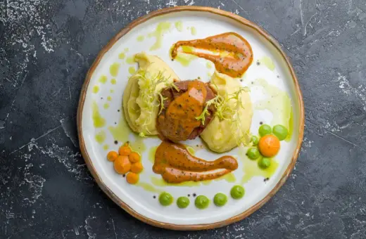 Mięso z puree ziemniaczanym, ozdobione pomarańczowym sosem do mielonych i zielonymi groszkami.