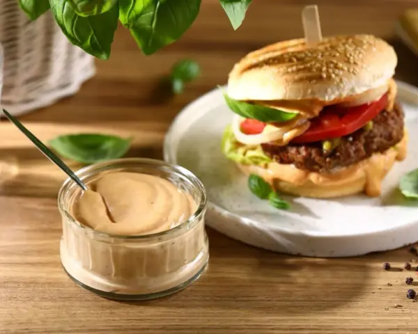 Pyszny sos do burgera w słoiczku, obok apetycznego burgera z dodatkami. Idealny do każdej kanapki.