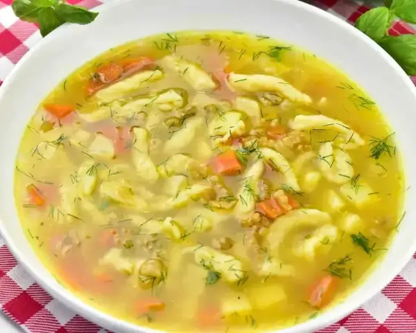 Aromaticzna zupa zacierkowa z kawałkami marchewki i świeżym koperkiem, podana w białej misce na czerwono-białej kratce.