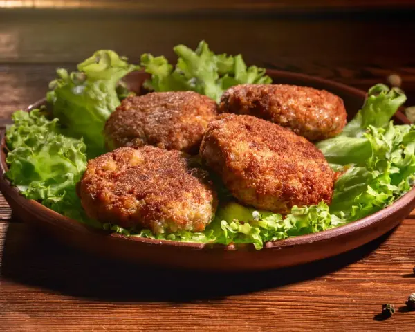 Cztery apetyczne kotlety mielone z airfryer, podane na liściach sałaty. Idealne na szybki obiad.