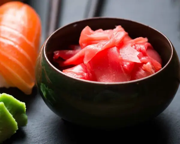 Miseczka z różowym, marynowanym imbirem obok sushi i wasabi. Idealny dodatek do japońskich potraw.
