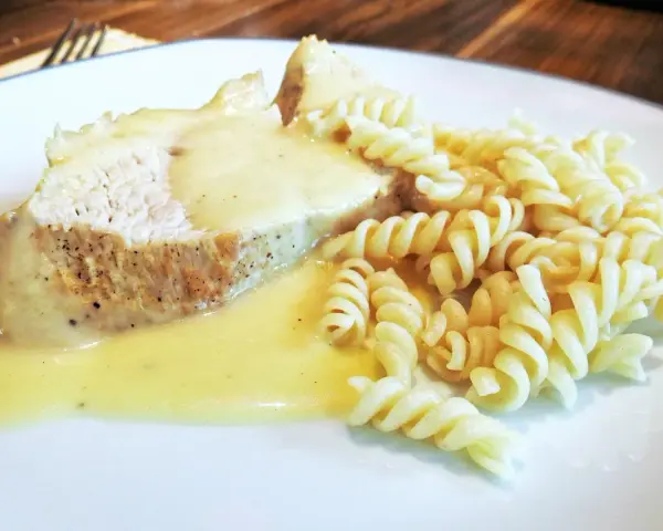 Kawałek pieczonego mięsa w kremowym sosie potrawkowym, podany z makaronem fusilli.