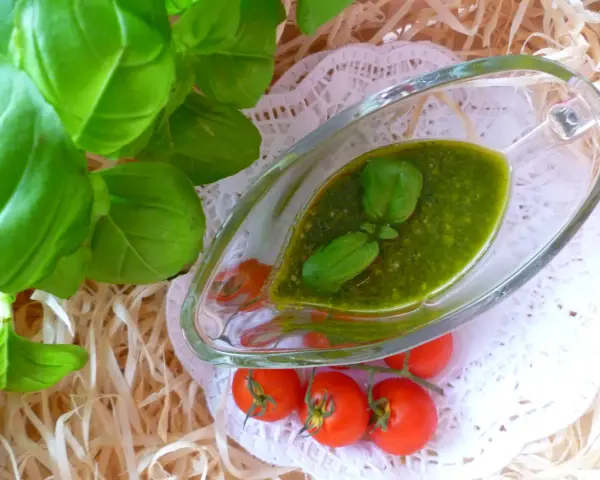 Świeże liście bazylii i pomidorki koktajlowe obok sosu pesto z bazylii w szklanym naczyniu.