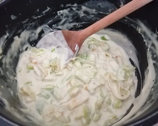 Kremowy sos porowy w garnku, mieszany drewnianą łyżką. Pyszny dodatek do obiadu.