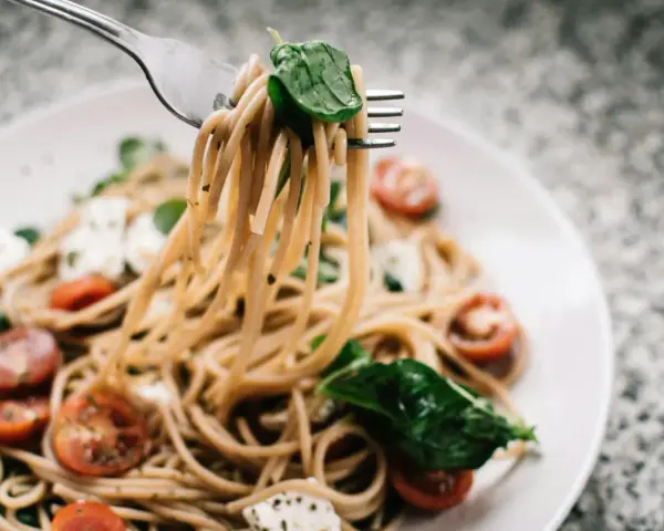Widelec podnosi porcję spaghetti z pomidorkami i mozzarellą. Czy makaron to węglowodany? Tak, to pyszne źródło energii!