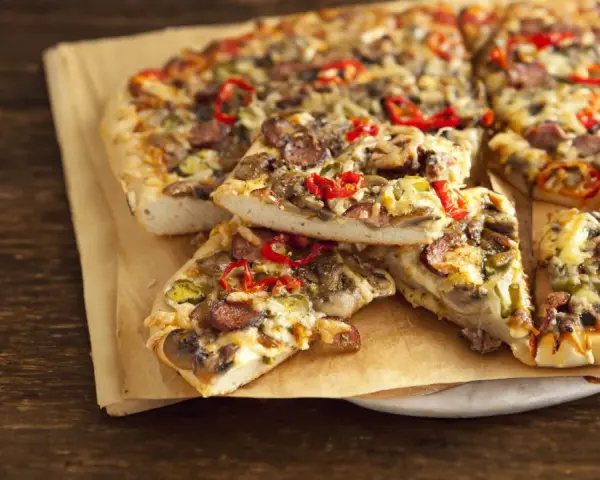 Grube ciasto na pizze z kiełbasą, pieczarkami i papryką, podane na papierze do pieczenia.