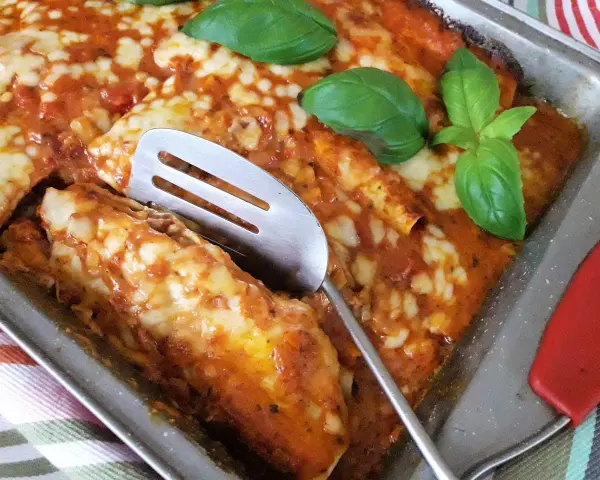 Zapiekana tortilla z mięsem mielonym, polana sosem pomidorowym i posypana serem, ozdobiona listkami bazylii.