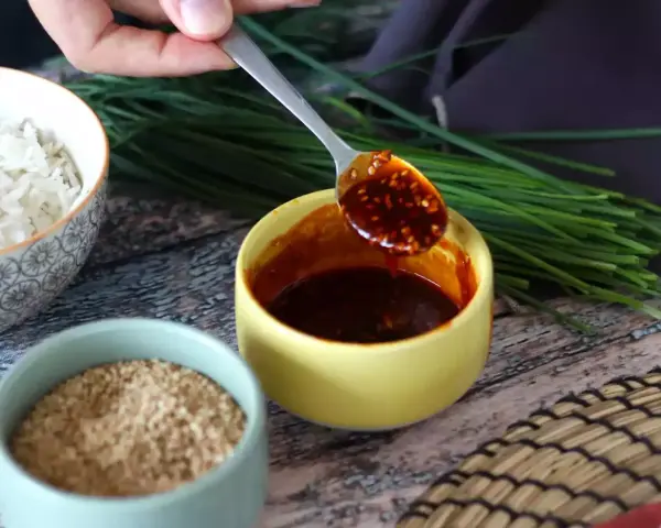 Łyżka z aromatycznym sosem gochujang, obok miseczki ryżu, sezamu i szczypiorku.