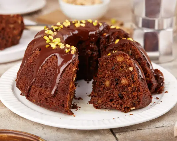 Wilgotna babka czekoladowa z orzechami, polana polewą i posypana pistacjami. Idealna na szybki deser.