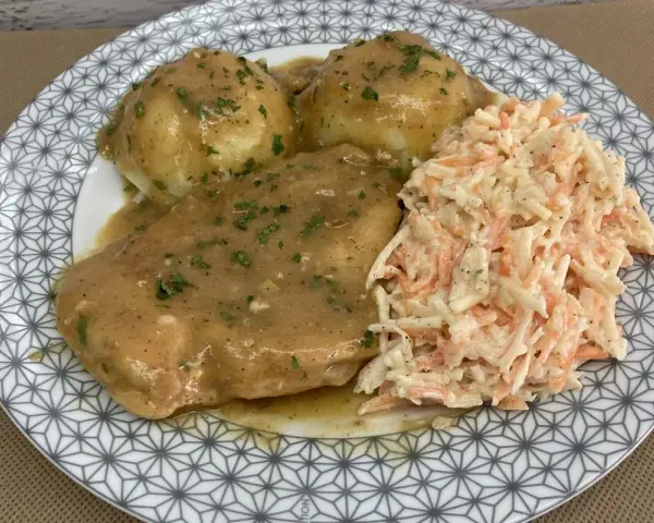 Pyszna pierś z kurczaka w sosie własnym, podana z ziemniakami i surówką z marchewki i kapusty.