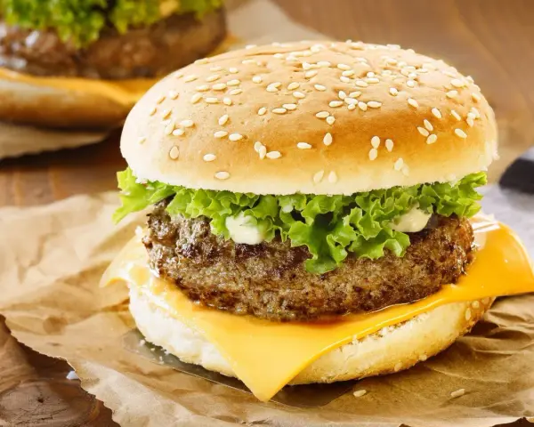 Zbliżenie na cheeseburgera z serem, sałatą i majonezem na bułce z sezamem.