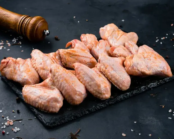 Skrzydełka kurczaka gotowe do pieczenia, zamarynowane w aromatycznej solance. Obok młynek do pieprzu i gruboziarnista sól.