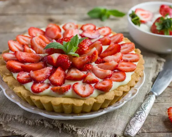 Tarta z truskawkami i kremem, ozdobiona listkami mięty.