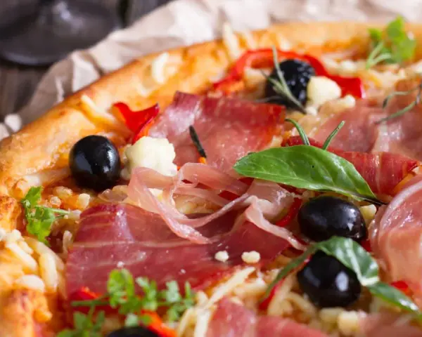 Pyszna pizza z cienko pokrojoną, aromatyczną szynką, czarnymi oliwkami i papryką. Idealna jaka szynka na pizzę!