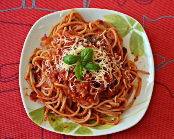 Pyszny sos do makaronu spaghetti z tartym serem i bazylią na talerzu.