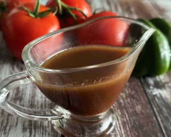 Sos balsamiczny w sosjerce, w tle pomidory i zielona papryka. Idealny do sałatek i mięs.