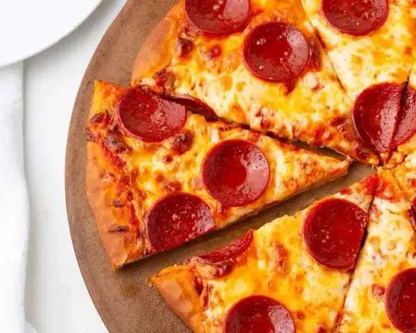 Kawałki pizzy z serem i okrągłymi plasterkami peperoni, ułożone na drewnianej desce.