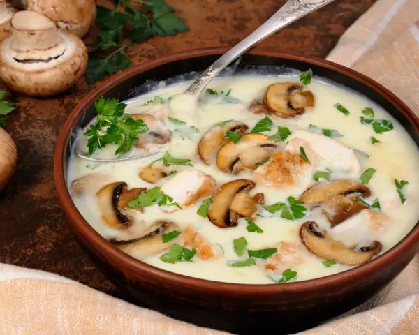 Kremowa zupa pieczarkowa przepis babci z kawałkami kurczaka i świeżą natką pietruszki. Obok miski leżą świeże pieczarki.