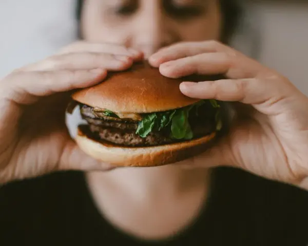 Osoba trzyma soczystego burgera, zastanawiając się, ile kalorii ma burger w restauracji.