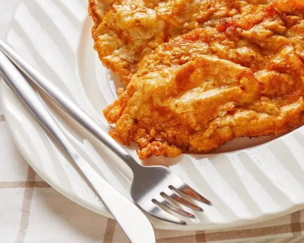 Złocisty kotlet słoneczny na białym talerzu, obok sztućce. Idealny na słoneczny dzień.
