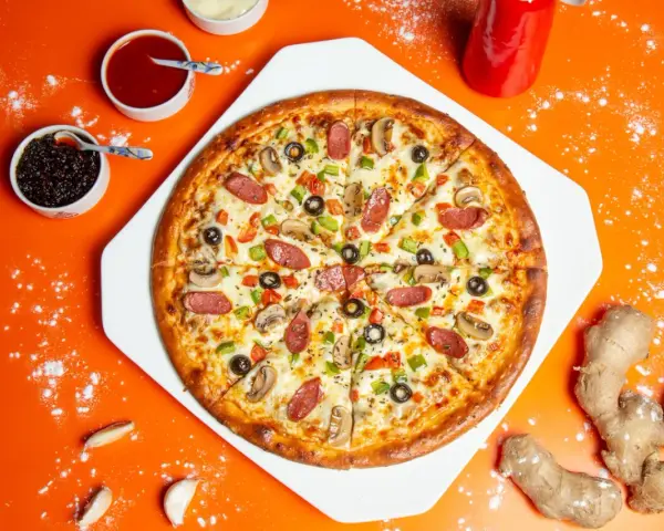 Pizza z kiełbasą, pieczarkami i oliwkami na pomarańczowym tle, obok sosy i imbir.