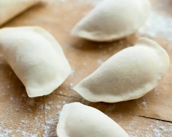 Surowe pierogi uformowane na drewnianej desce. To ciasto na pierogi bez jajka, gotowe do nadzienia.